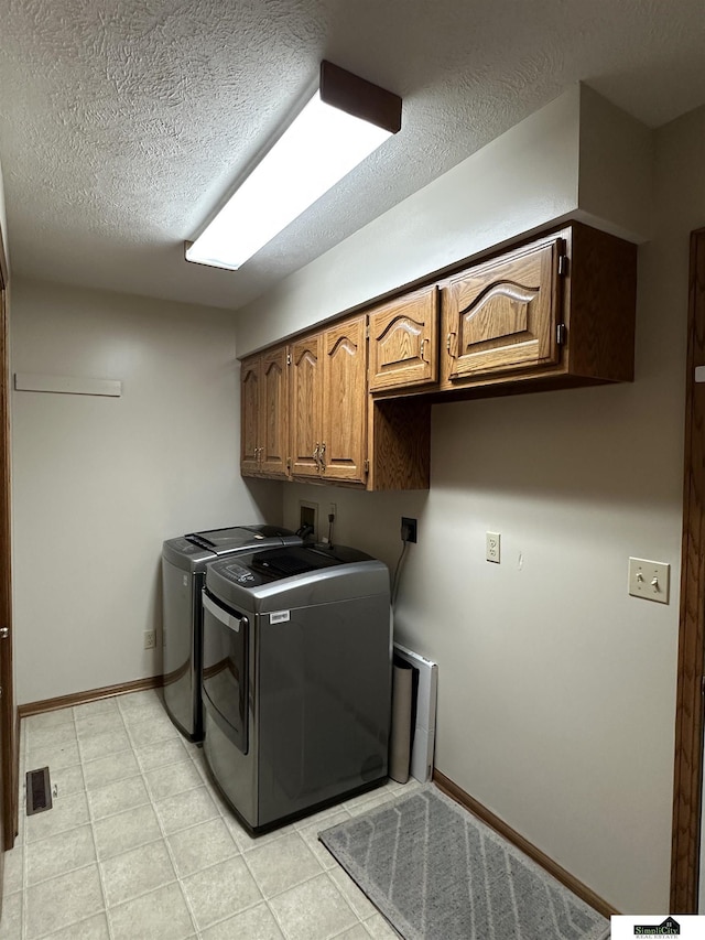 laundry room with cabinets, a textured ceiling, and washing machine and clothes dryer