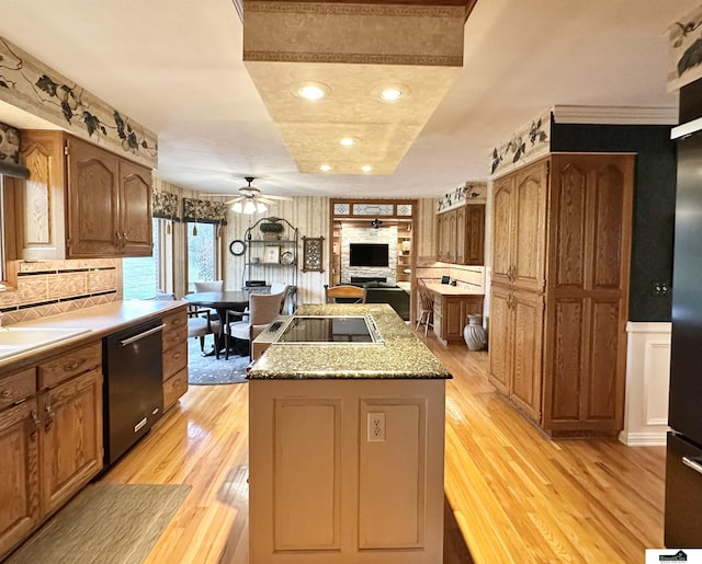 kitchen featuring black appliances, a raised ceiling, ceiling fan, light wood-type flooring, and a kitchen island