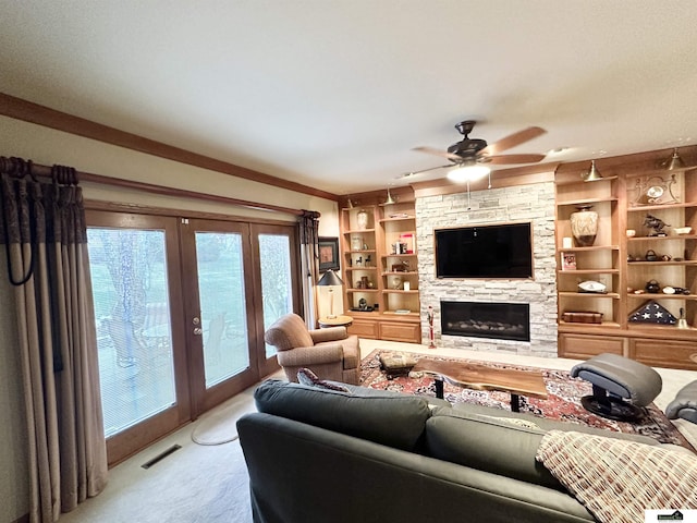 living room featuring french doors, a stone fireplace, crown molding, built in shelves, and light colored carpet