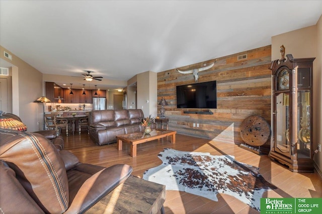 living room with wood walls, ceiling fan, and light hardwood / wood-style floors