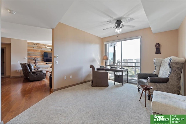 sitting room with carpet flooring, ceiling fan, and wooden walls