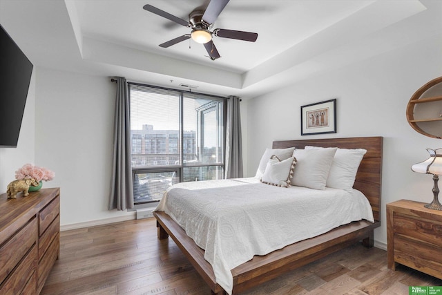 bedroom with ceiling fan, dark hardwood / wood-style flooring, and a tray ceiling