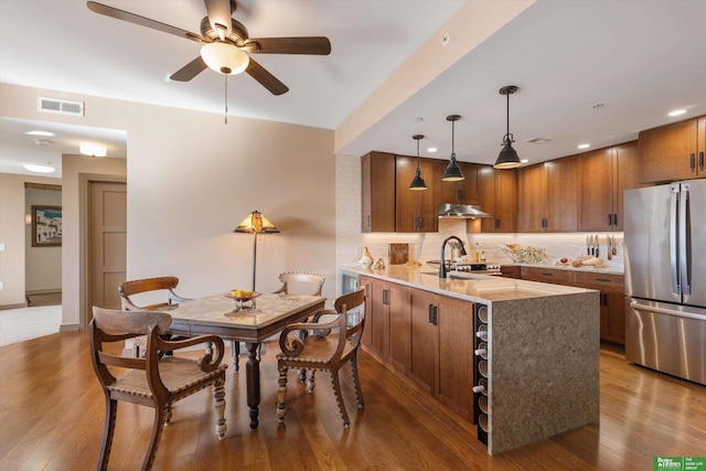 kitchen with light stone countertops, dark hardwood / wood-style flooring, backsplash, decorative light fixtures, and stainless steel refrigerator