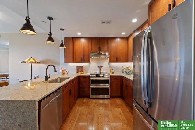 kitchen with sink, stainless steel appliances, light hardwood / wood-style flooring, kitchen peninsula, and decorative light fixtures