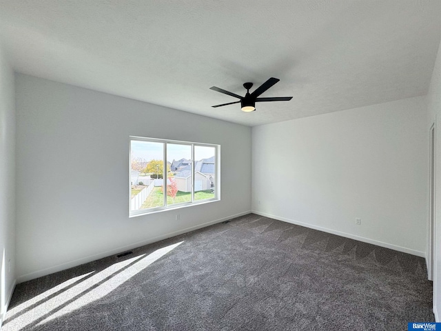 unfurnished room with ceiling fan, dark carpet, and a textured ceiling