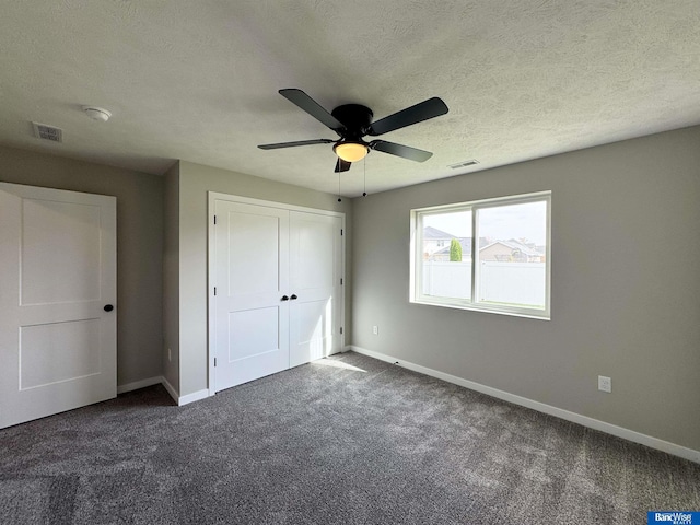 unfurnished bedroom with ceiling fan, a closet, a textured ceiling, and dark colored carpet