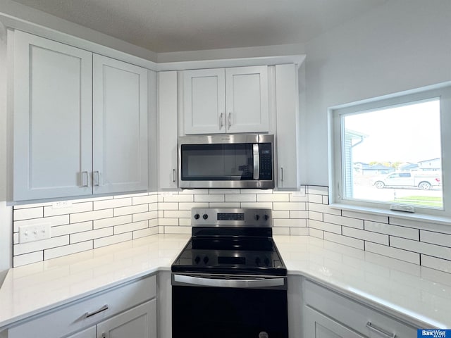 kitchen featuring appliances with stainless steel finishes, backsplash, white cabinetry, and light stone counters