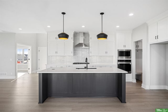 kitchen with pendant lighting, a center island with sink, white cabinets, wall chimney exhaust hood, and stainless steel appliances