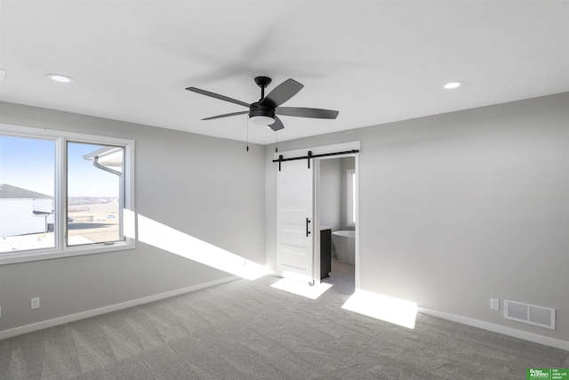 unfurnished bedroom featuring carpet, ceiling fan, a barn door, and ensuite bathroom