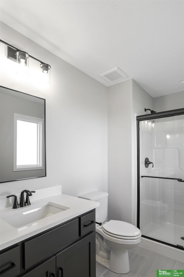 bathroom featuring a textured ceiling, vanity, toilet, and walk in shower