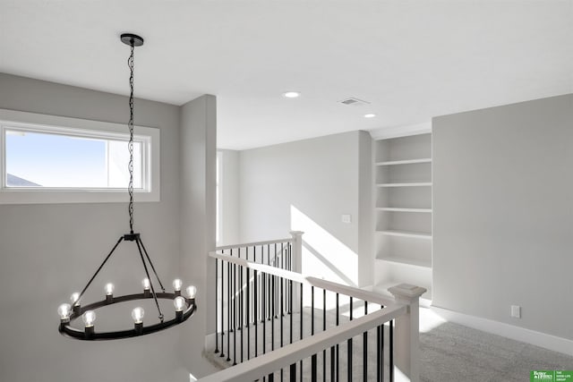 corridor featuring carpet flooring, a notable chandelier, and built in shelves