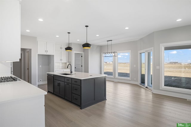 kitchen featuring white cabinets, sink, an island with sink, and hanging light fixtures