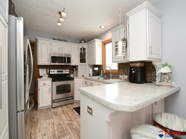 kitchen with kitchen peninsula, appliances with stainless steel finishes, tasteful backsplash, a kitchen bar, and white cabinetry