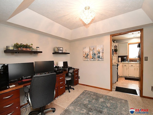 carpeted office featuring sink, a textured ceiling, and a tray ceiling