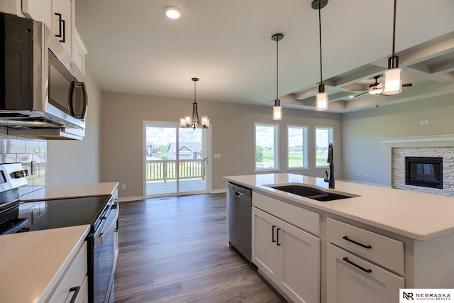 kitchen featuring appliances with stainless steel finishes, coffered ceiling, sink, white cabinetry, and an island with sink