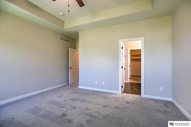 unfurnished bedroom featuring ceiling fan, a tray ceiling, a walk in closet, light carpet, and a closet