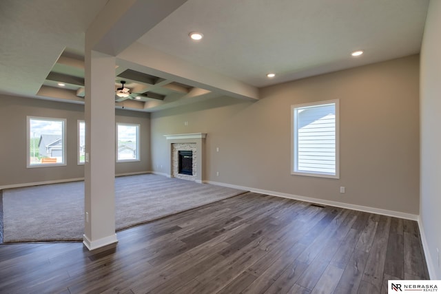 unfurnished living room with beam ceiling, dark hardwood / wood-style floors, a stone fireplace, and ceiling fan