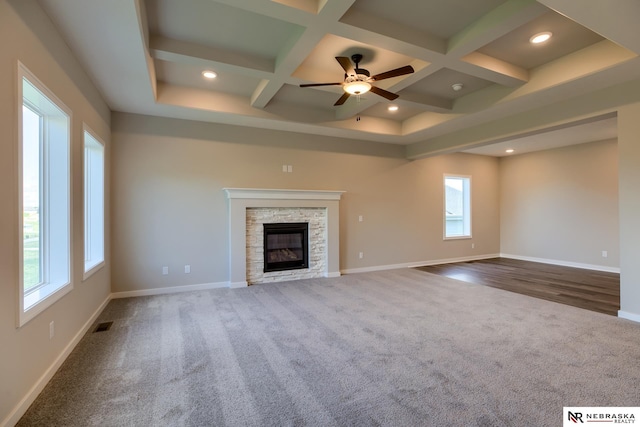 unfurnished living room featuring ceiling fan, coffered ceiling, a stone fireplace, beamed ceiling, and carpet floors