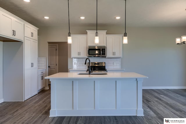 kitchen with decorative light fixtures, stainless steel appliances, white cabinetry, and a kitchen island with sink