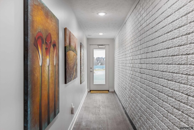 hallway featuring hardwood / wood-style floors, a textured ceiling, and brick wall