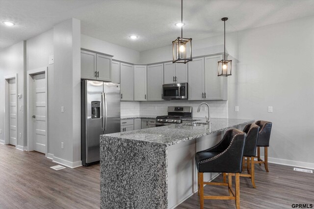 kitchen featuring backsplash, stone counters, decorative light fixtures, kitchen peninsula, and stainless steel appliances