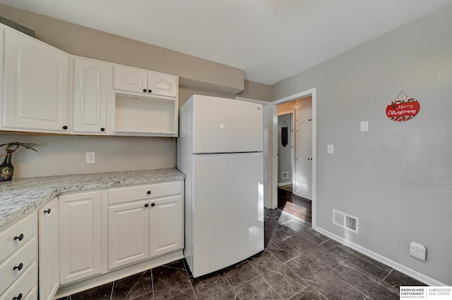 kitchen featuring white cabinetry, white fridge, and light stone countertops