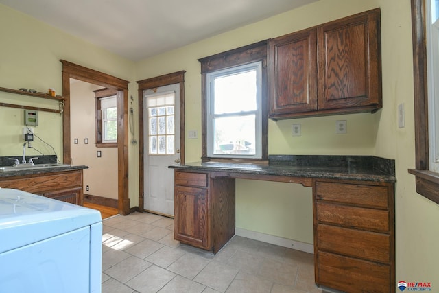 kitchen with sink, dark stone countertops, washer / dryer, light tile patterned floors, and built in desk