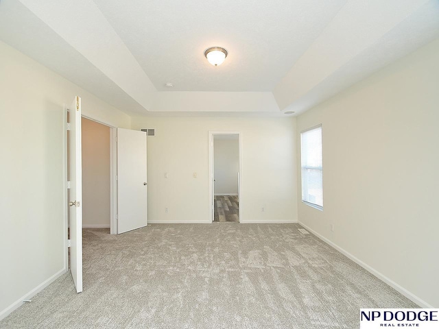 unfurnished bedroom with a raised ceiling, a walk in closet, and light carpet