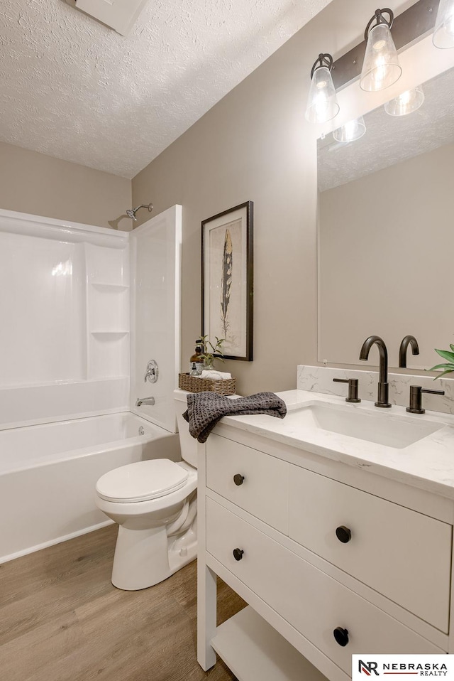 full bathroom with tub / shower combination, hardwood / wood-style floors, a textured ceiling, toilet, and vanity