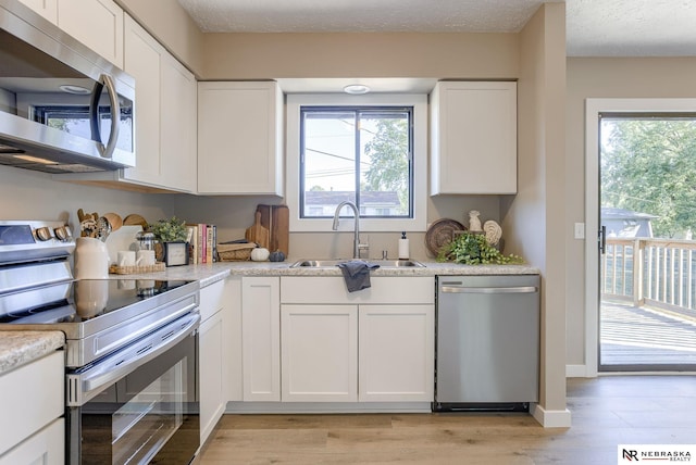 kitchen featuring white cabinets, sink, light stone countertops, appliances with stainless steel finishes, and light hardwood / wood-style floors