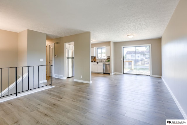 empty room with sink, light wood-type flooring, and a textured ceiling