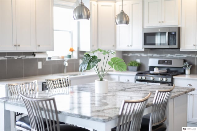 kitchen with stainless steel appliances, a kitchen breakfast bar, light stone counters, decorative light fixtures, and white cabinets