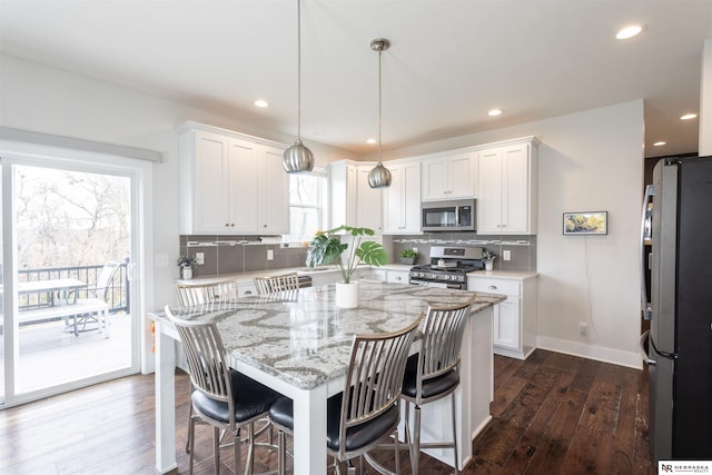 kitchen featuring plenty of natural light, white cabinets, stainless steel appliances, and decorative light fixtures