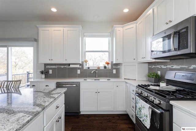 kitchen with light stone countertops, appliances with stainless steel finishes, tasteful backsplash, sink, and white cabinets