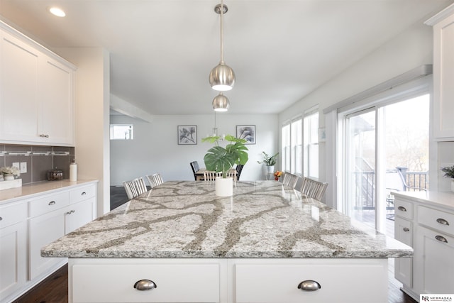 kitchen with a breakfast bar, a center island, white cabinets, decorative light fixtures, and light stone counters