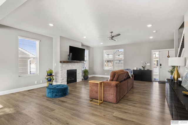 living room with hardwood / wood-style flooring, ceiling fan, and a stone fireplace