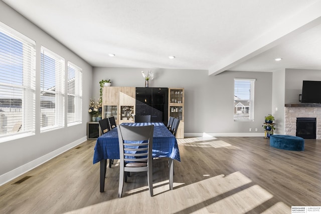 dining room featuring beam ceiling, a fireplace, a healthy amount of sunlight, and light hardwood / wood-style floors