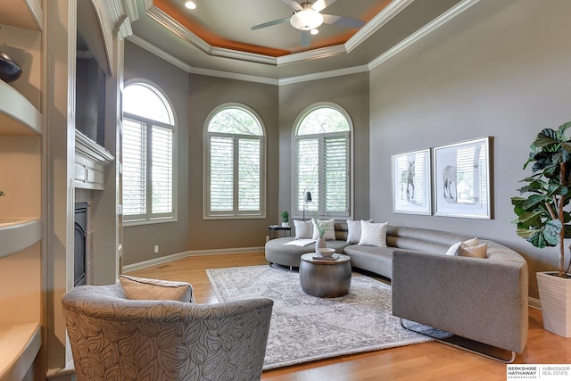 living room with ceiling fan, light wood-type flooring, crown molding, and a tray ceiling