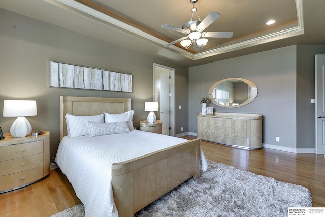 bedroom with hardwood / wood-style flooring, ceiling fan, crown molding, and a tray ceiling