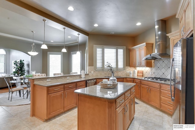 kitchen featuring pendant lighting, a center island, stainless steel appliances, and wall chimney range hood