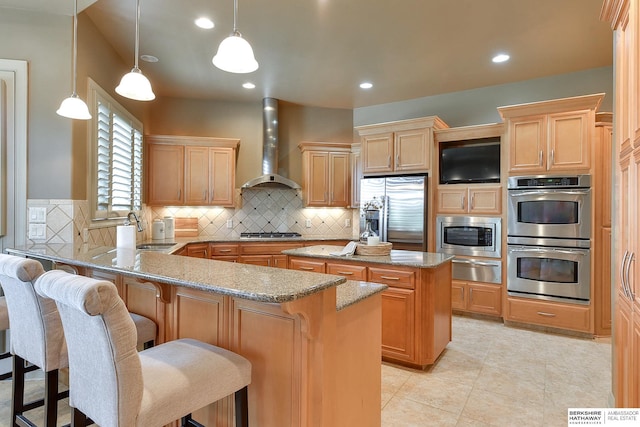 kitchen with kitchen peninsula, appliances with stainless steel finishes, sink, wall chimney range hood, and a breakfast bar area