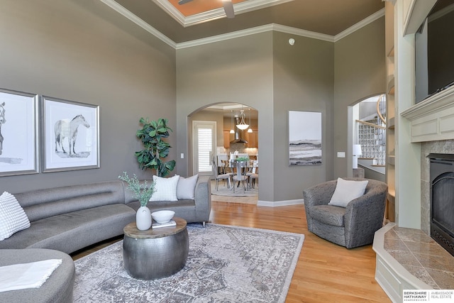 living room featuring a tiled fireplace, hardwood / wood-style floors, a high ceiling, and ornamental molding