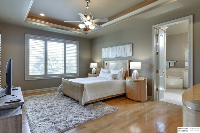 bedroom featuring a raised ceiling, crown molding, ensuite bath, ceiling fan, and light hardwood / wood-style floors