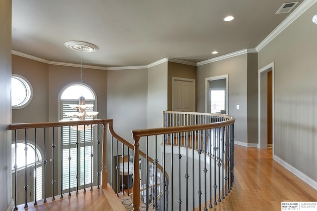 corridor with light wood-type flooring, crown molding, a wealth of natural light, and a chandelier