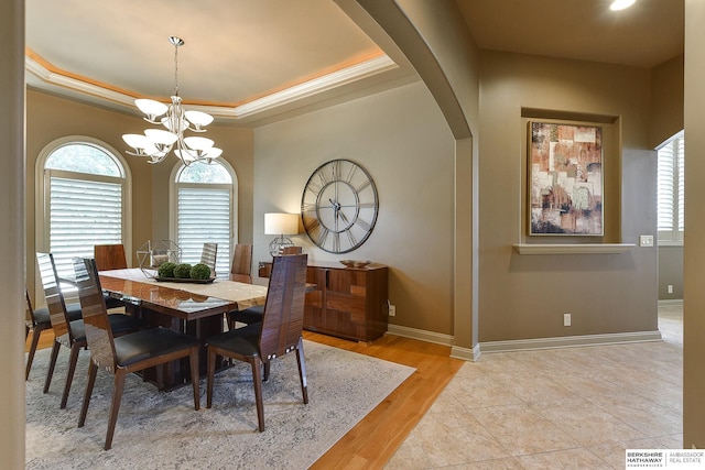 dining space featuring a raised ceiling, crown molding, light hardwood / wood-style flooring, and an inviting chandelier