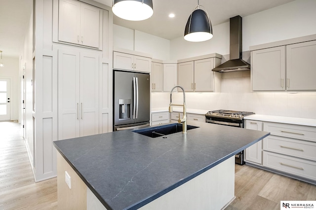 kitchen with sink, wall chimney range hood, appliances with stainless steel finishes, and a kitchen island with sink