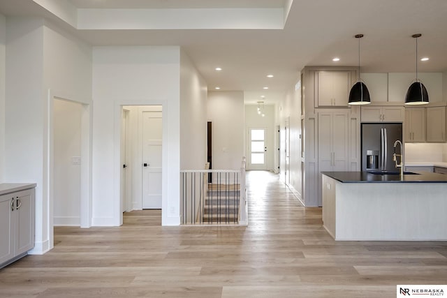 kitchen with hanging light fixtures, sink, light wood-type flooring, and stainless steel fridge with ice dispenser