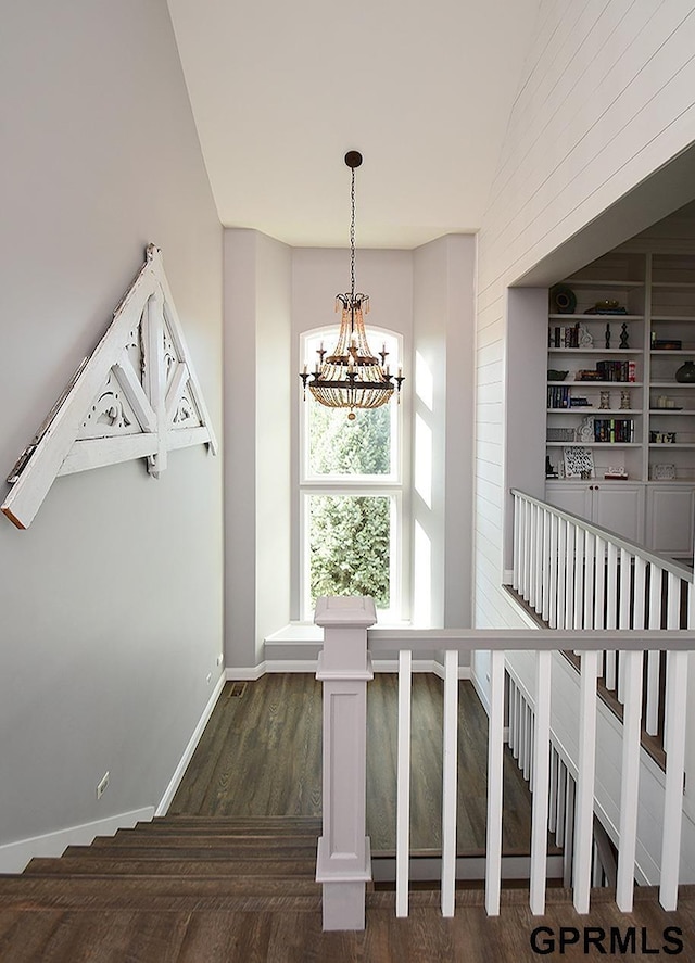 staircase featuring hardwood / wood-style floors, built in features, a notable chandelier, and a high ceiling