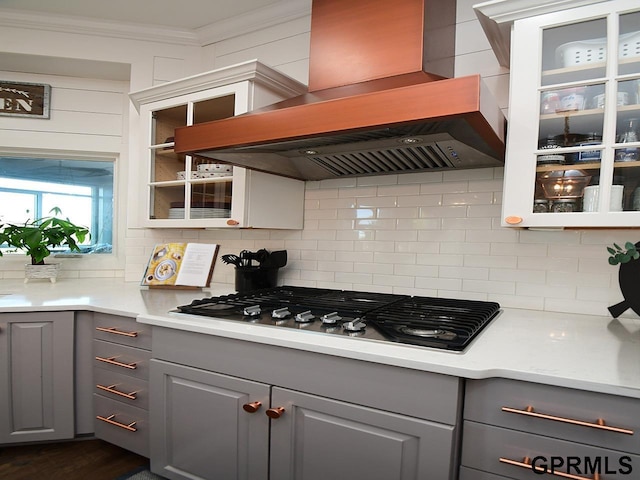 kitchen featuring gray cabinetry, backsplash, crown molding, custom range hood, and stainless steel gas cooktop