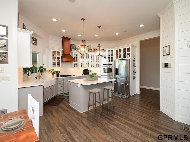 kitchen with premium range hood, stainless steel appliances, sink, decorative light fixtures, and a center island